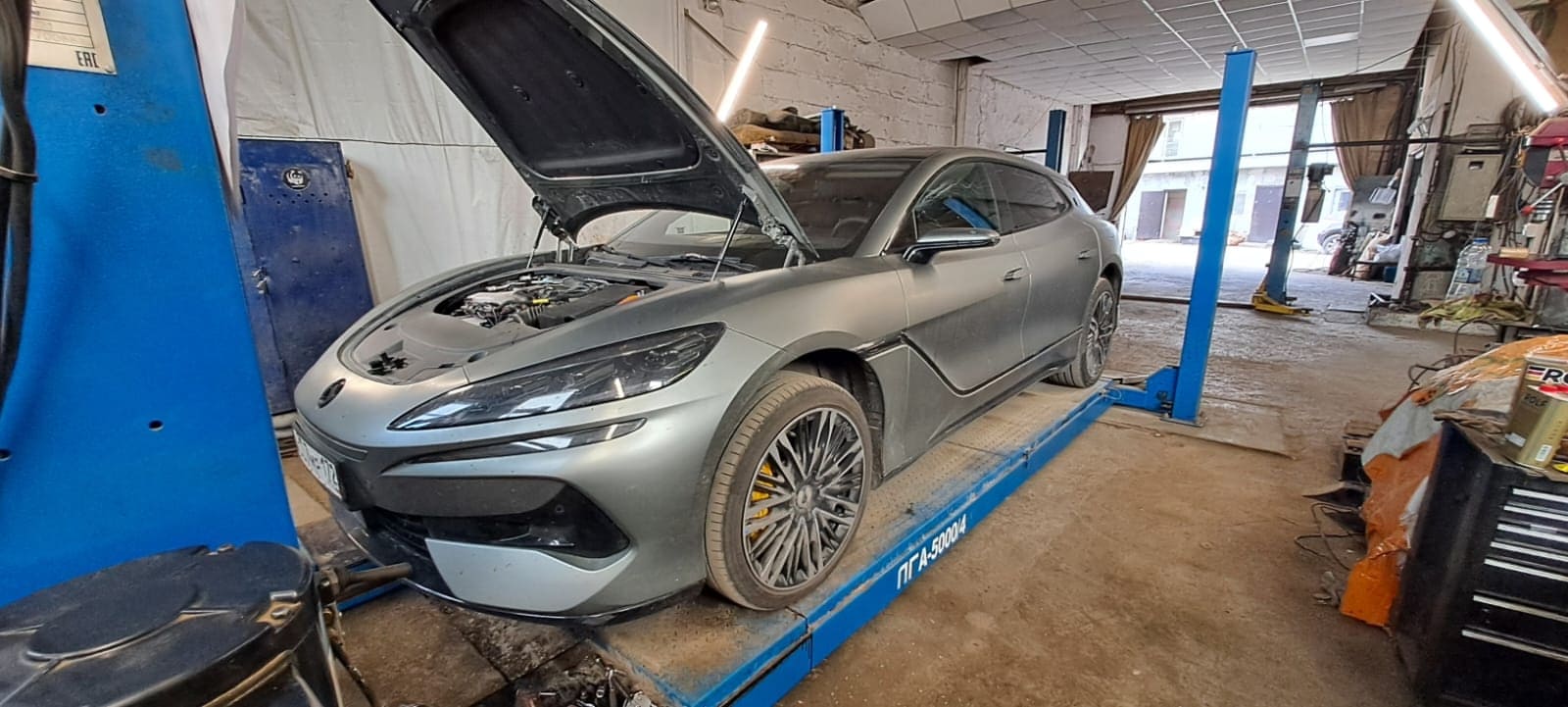 Серебристый BYD Denza Z9 GT с открытым капотом на подъемнике